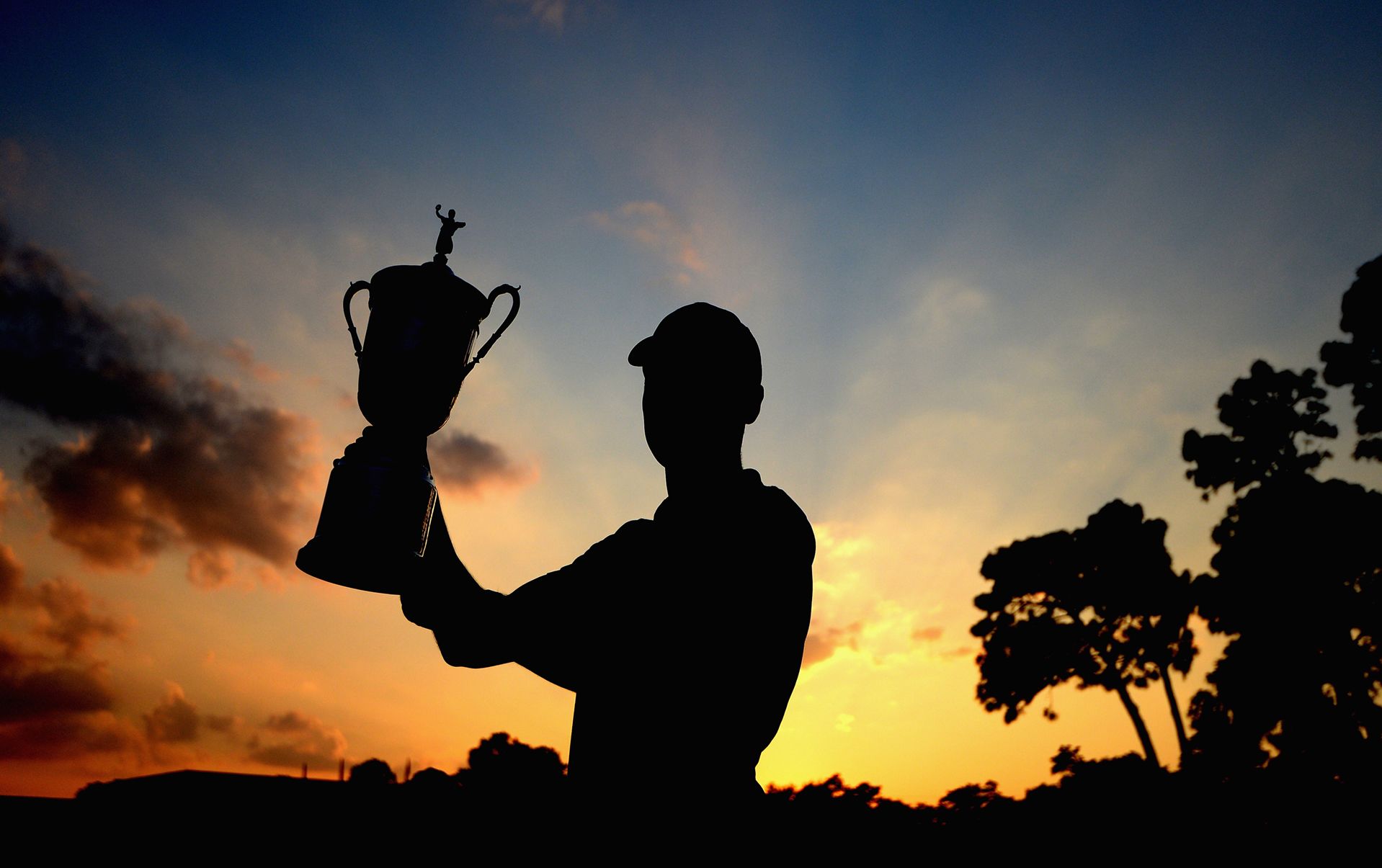 A Man Standing In Front Of A Sunset Holding A Trophy